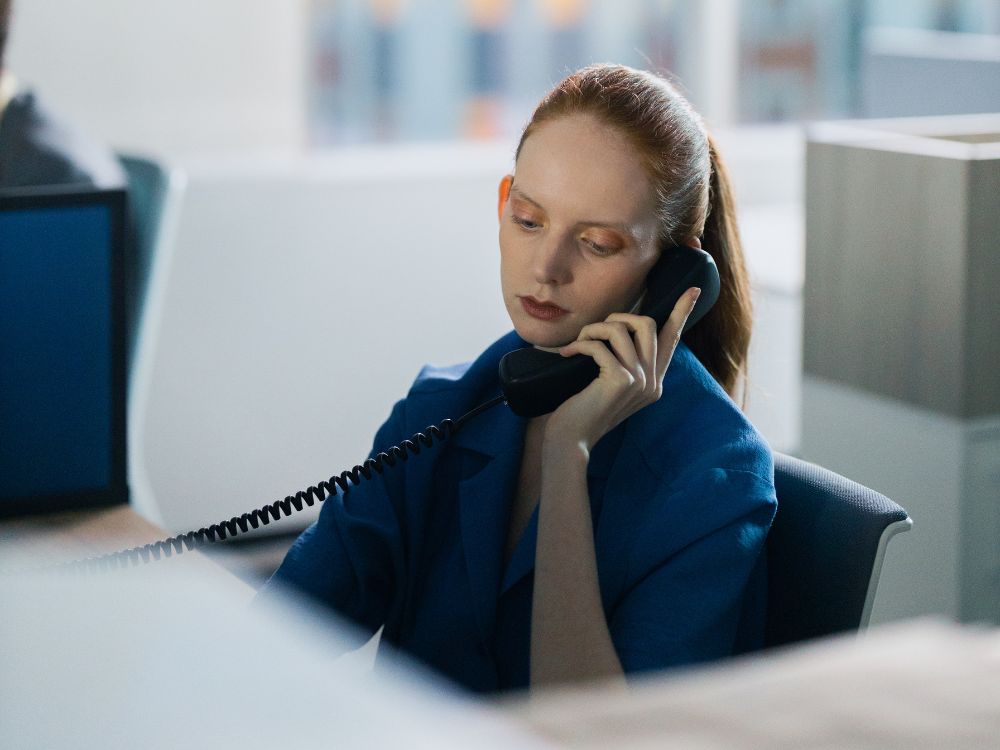 Mulher atendendo ligação telefônica em ambiente corporativo, concentrada em sua estação de trabalho dentro de um escritório moderno.