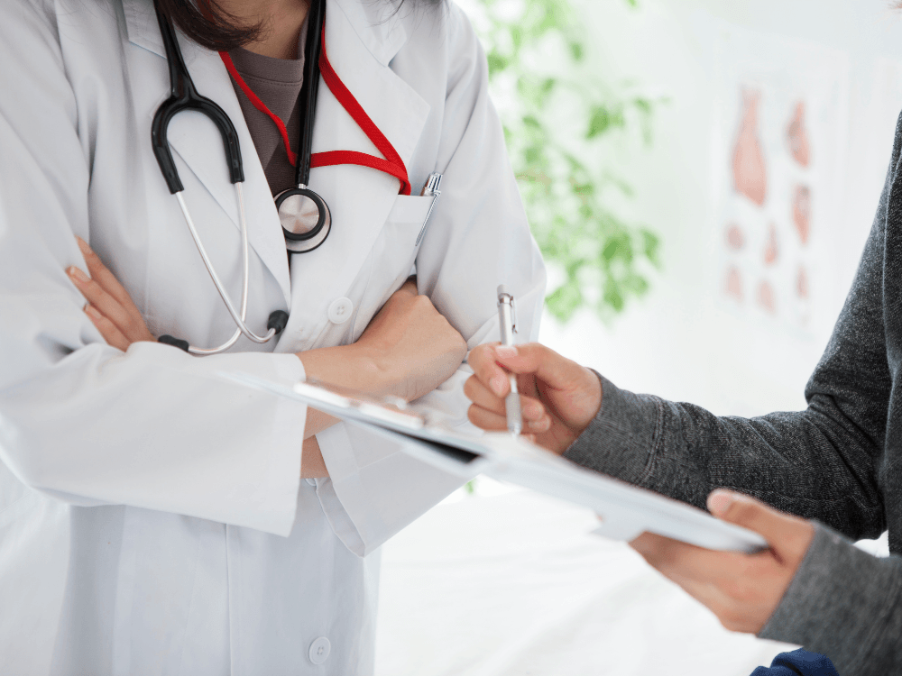 Médica conversando com atendente, enquanto essa última escreve em uma prancheta